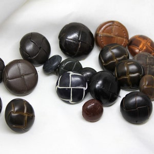May include: A collection of brown, black, and tan leather buttons with a woven design. The buttons are various sizes and shapes.