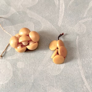 May include: Two clusters of beige buttons, each with a different arrangement. The buttons are round and have a smooth, slightly shiny finish.