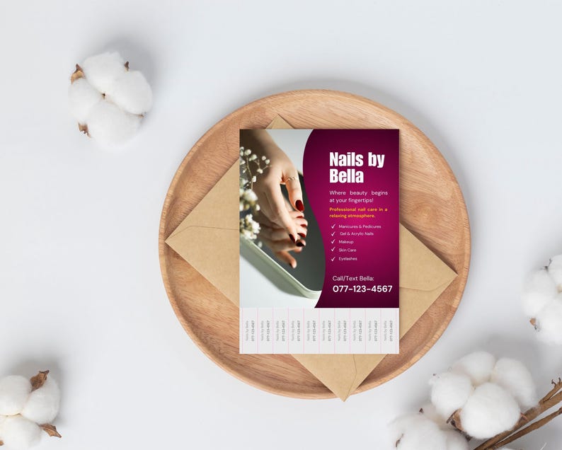 May include: A business card for "Nails by Bella" with a burgundy and white design, featuring a hand with red nail polish reflected in a mirror. The card is on a wooden plate with a brown envelope and cotton accents.
