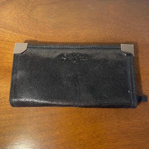 May include: Black wallet with silver corner accents. The wallet has a textured surface and the Jessica Simpson logo is embossed on the front. The wallet is rectangular and appears to be made of leather.