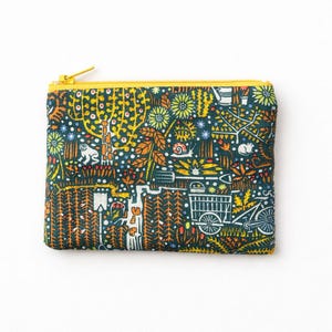 May include: A small, rectangular pouch with a yellow zipper. The pouch is covered in a whimsical, colorful pattern featuring trees, animals, and a bicycle. The background is a dark teal color.