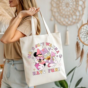 Op de afbeelding: Cr&egrave;mekleurige draagtas met een afbeelding van Minnie Mouse en Daisy Duck met zonnebrillen en ijs. De tekst "GIRLS JUST WANNA HAVE FUN!" is gedrukt in een retro lettertype. De tas heeft witte handvatten.