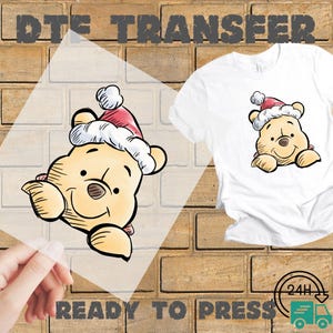 May include: A white t-shirt featuring a cartoon illustration of a bear wearing a Santa hat. The image is a DTE transfer, with the words "READY TO PRESS" printed below. The background is a brick wall.