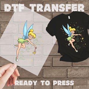 May include: DTF transfer featuring a cartoon fairy with blonde hair, blue wings, and a green dress. The text "All You Need Is Faith, Trust, And Pixie Dust" is included. A black t-shirt with the same design is also shown. The words "READY TO PRESS" are at the bottom.