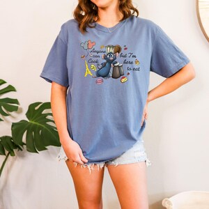 May include: A blue t-shirt featuring a cartoon rat chef with the text "Anyone can cook but I'm here to eat." The design includes a chef's hat, Eiffel Tower, and food illustrations. The shirt is a relaxed fit.
