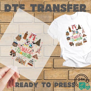 May include: A white t-shirt with a "World Traveler" graphic featuring Mickey and Minnie Mouse, surrounded by iconic landmarks like the Eiffel Tower and Japanese Torii gates. A clear DTE transfer with the same design is held in front of the shirt. The words "READY TO PRESS" are visible.