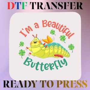 May include: A DTF transfer sheet featuring a cartoon yellow caterpillar with orange wings, surrounded by green four-leaf clovers. The text reads I'm a Beautiful BUTTERFLY in red and teal. The top says DTF TRANSFER and the bottom READY TO PRESS.
