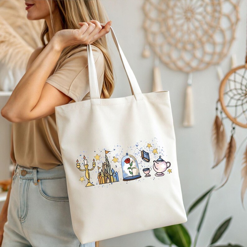 K&ouml;nnte beinhalten: Cremefarbene Tragetasche mit einer farbenfrohen Illustration eines Schlosses, einer Rose, einer Teekanne und anderen m&auml;rchenhaften Elementen. Die Tasche hat lange Henkel und wird von einer Person getragen.