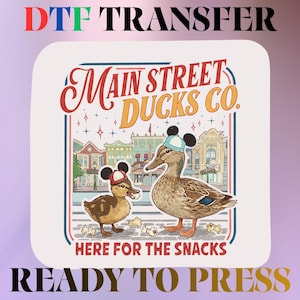 May include: A DTF transfer featuring a graphic of two brown ducks wearing mouse-ear hats in front of a street scene. The text reads Main Street Ducks Co. and Here for the Snacks. The design is ready to press for apparel customization projects.