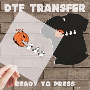 May include: A black t-shirt with a Halloween design featuring an orange pumpkin and three white ghosts. The words "DTF TRANSFER" and "READY TO PRESS" are printed on the image.