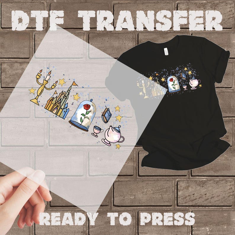 K&ouml;nnte beinhalten: Schwarzes T-Shirt mit einem DTF-Transferdesign mit einer Rose in einer Glaskuppel, einem Schloss, einer Teekanne und anderen M&auml;rchenelementen. Die W&ouml;rter "DTF TRANSFER" und "READY TO PRESS" sind sichtbar.
