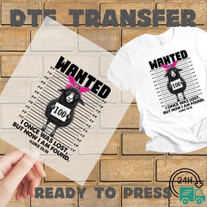 May include: A white t-shirt and a ready-to-press transfer sheet featuring a black sheep wearing a pink headband. The sheep is depicted in a mugshot style with the word "WANTED" above it and the text "I ONCE WAS LOST, BUT NOW I AM FOUND."