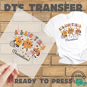 May include: White t-shirt with a colorful graphic that says "ALL ABOUT FALL" and features cartoon pumpkins and leaves. A clear transfer sheet with the same design is held in front of the shirt. The words "READY TO PRESS" are at the bottom.