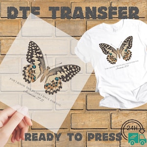 May include: A white t-shirt with a butterfly graphic and the text "FOR I KNOW THE PLANS I HAVE FOR YOU Jeremiah 29:11". A ready-to-press DTE transfer with the same butterfly design is also shown. The image is set against a brick wall.