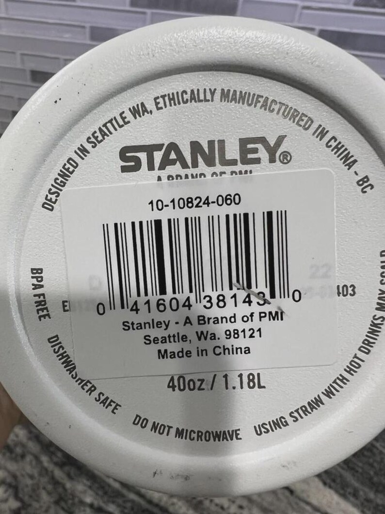 K&ouml;nnte beinhalten: Wei&szlig;e Wasserflasche der Marke Stanley mit Etikett. Das Etikett enth&auml;lt den Text "Designed in Seattle WA, Ethically Manufactured in China - BC", das Stanley-Logo und einen Barcode. Die Flasche ist 1,18 l und BPA-frei.