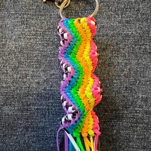 May include: A rainbow-colored keychain made from woven plastic bands. The keychain has a silver key ring and a black and white checkered pattern.