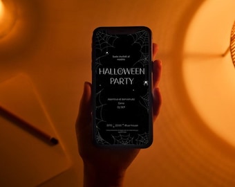 May include: A smartphone displays a Halloween Party invitation with spiderweb graphics and the text "Halloween Party". The phone is held in a hand, with a candle, notepad, and lamp in the warm-toned background.