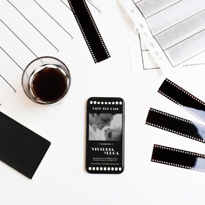 May include: A black and white save the date card on a smartphone with a photo of a couple. The card has a film strip border and the text "Save the Date" and "Victoria + Luca".