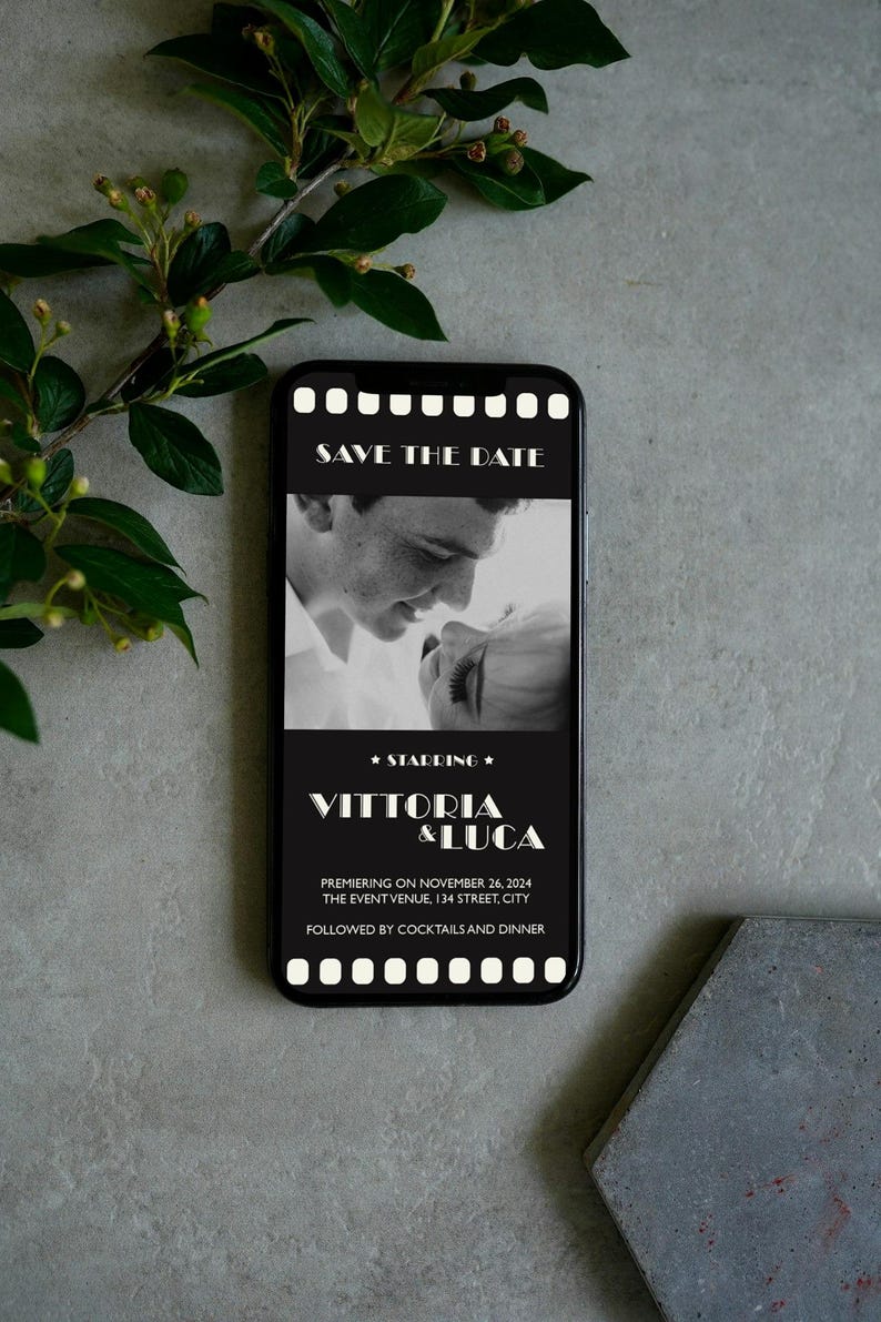 May include: Black and white photo of a couple on a smartphone screen with a film strip border. The text "Save the Date" is at the top of the screen. The text "Starring Vittoria & Luca" is below the photo. The text "Premiering on November 26, 2024 The Event Venue, 134 Street, City" is below the names. The text "Followed by Cocktails and Dinner" is at the bottom of the screen.