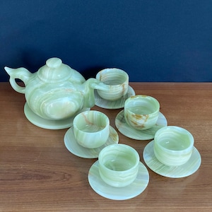 Op de afbeelding: Een groene onyx theeset met een theepot en vijf kopjes en schoteltjes. De set is gemaakt van gepolijst groene onyx met bruine en witte marmering.