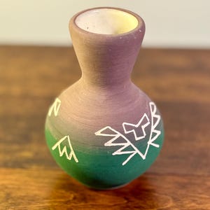 Peut inclure: Petit vase artisanal au design unique. Le vase présente un dégradé de couleurs, passant du vert au violet. Des formes géométriques blanches ornent la surface du vase. L'intérieur est de couleur jaune clair.