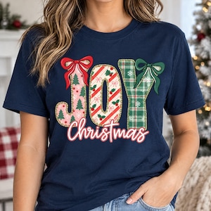 May include: A navy blue short-sleeve t-shirt featuring the word JOY in large, decorative letters. The J is pink with green trees, the O is red and white striped with holly, and the Y is green plaid with snowflakes. The word Christmas is written below.