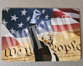 Puede incluir: Una persona levanta el puño en el aire frente a una bandera estadounidense y un documento con el texto "We the People".