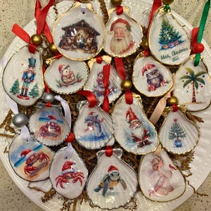 May include: A collection of seashell Christmas ornaments with gold trim and red ribbons. Each ornament features a different festive design, including a nativity scene, Santa Claus, a Christmas tree, and a nutcracker.