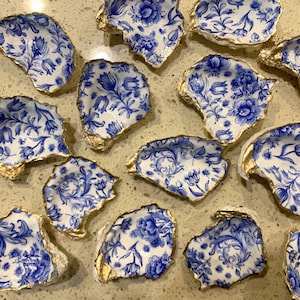 May include: A collection of blue and white oyster shells with gold accents. The shells are decorated with a floral pattern and are perfect for displaying small items.