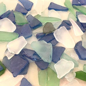 May include: A collection of sea glass pieces in various shapes and sizes. The colors include shades of blue, green, and white. The pieces are scattered, creating a textured and natural aesthetic. Ideal for crafts or decorative purposes.