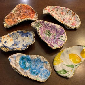 May include: Six oyster shells with gold trim, each decorated with a different floral pattern. The patterns include orange, pink, purple, blue, and yellow flowers.