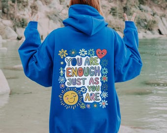 May include: A royal blue hoodie with a colorful graphic on the back that says "You are enough just as you are". The graphic features a sun, a heart, and flowers.