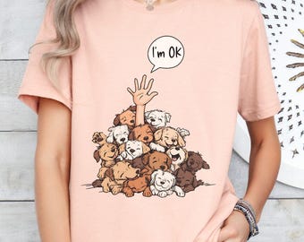 Peut inclure: T-shirt rose clair avec un motif de chiots empilés, une main tendue vers le haut et une bulle de dialogue disant « I'm OK ». Les chiots sont de différentes nuances de marron et de blanc.