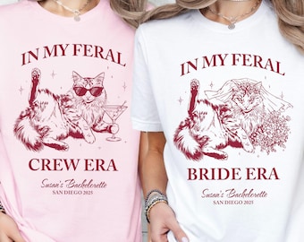 May include: Two t-shirts, one pink and one white, with a cat graphic. The pink shirt says "IN MY FERAL CREW ERA" and the white shirt says "IN MY FERAL BRIDE ERA". Both shirts have "Susan's Bachelorette SAN DIEGO 2025" printed below.