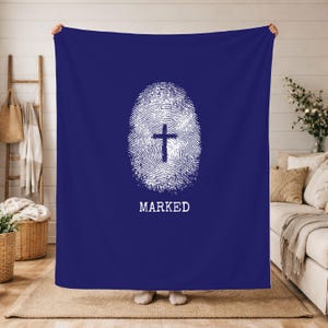 May include: A navy blue blanket featuring a white fingerprint design with a cross at its centre. The word "MARKED" is printed in white beneath the fingerprint. The blanket is held up by two people.