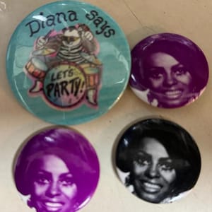May include: Four round buttons with different designs. The first button is turquoise blue with a cartoon illustration of a cat playing drums with the text "Diana Says Let's Party!" The other three buttons are purple, black, and white with a photo of a woman with dark hair and a white shirt.