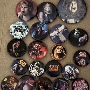 May include: A collection of nineteen circular pin-back buttons featuring various photographic and graphic images of Ozzy Osbourne and his band members. The buttons display diverse portraits, album art, and band logos in a variety of colors.