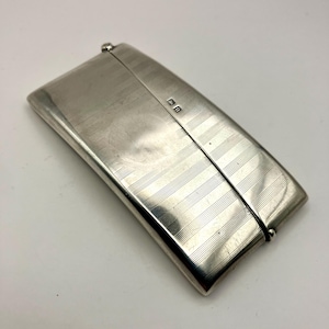 May include: A silver, rectangular, hinged box with a textured, striped pattern. The box has a small, square mark on the top.
