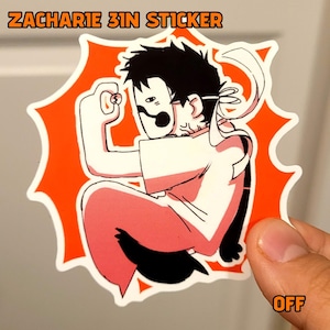 以下が含まれることがあります： 格闘ポーズの人物の漫画イラストが描かれた7.6cmのステッカー。キャラクターはマスクと白い衣装を着ており、オレンジ色の背景になっています。ステッカーの上部には「ZACHARIE 3IN STICKER」、下部には「OFF」と書かれています。