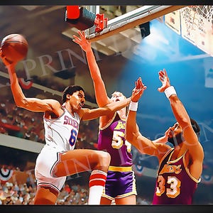 May include: A framed print of a basketball game in action. A player in a white jersey with the number 6 is about to shoot the ball, while two other players in purple jerseys attempt to block the shot. The image is set in a basketball arena.