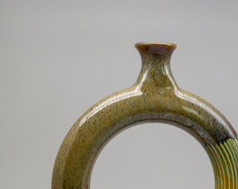 May include: A ceramic vase with a ring-shaped body and a green and brown glaze. The vase has a small, round base.