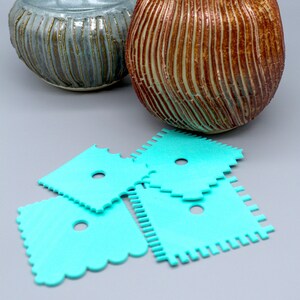 Puede incluir: Dos jarrones de cerámica con superficies texturizadas. El jarrón de la izquierda es azul y verde, el jarrón de la derecha es marrón y blanco. Tres herramientas de plástico turquesa para cerámica están en primer plano.