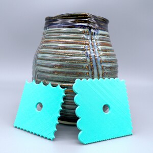 Puede incluir: Dos herramientas de cerámica azul turquesa con bordes festoneados y un agujero en el centro. Las herramientas se utilizan para alisar y dar forma a la arcilla.