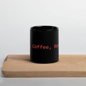 Op de afbeelding: Zwarte koffiemok met de tekst "Coffee, Repeat" in rood.