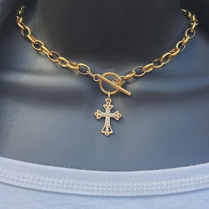 May include: A gold chain necklace with a toggle clasp and a small cross pendant encrusted with clear rhinestones.