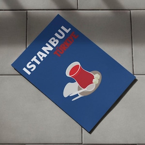 May include: A blue poster with the text "ISTANBUL TURKIYE" in white and red letters. The poster features a red teacup with sugar cubes on a white saucer.