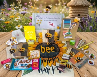 May include: A mystery box set featuring a Bee VIP Mystery Book Box, a yellow Never Give Up notebook, a sunflower-themed cloth with the text bee happy, an Aero chocolate bar, a Galaxy chocolate bar, bee-themed stickers, cards, and stationery.