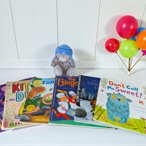 May include: A collection of children's books with colorful covers, including titles like "Don't Call Me Sweet!" and "The Gruffalo." A small teddy bear wearing a blue hat sits among the books. A cluster of colorful balloons adds a festive touch.