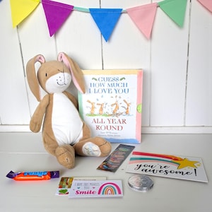 May include: A plush brown bunny toy sits next to a children's book titled "Guess How Much I Love You". Other items include a bookmark, a candy bar, a card that says "you're awesome!", and a card with a rainbow.