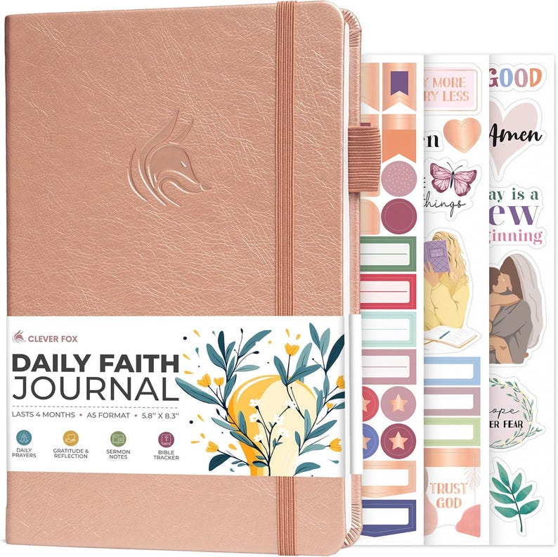 May include: A rose gold Daily Faith Journal with a fox logo embossed on the cover, an elastic closure, and a pen loop. The journal includes a paper band with floral illustrations and text, plus three sheets of decorative stickers with faith-themed designs.